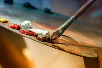 A close up photograph of a paintbrush picking up paint on a palette